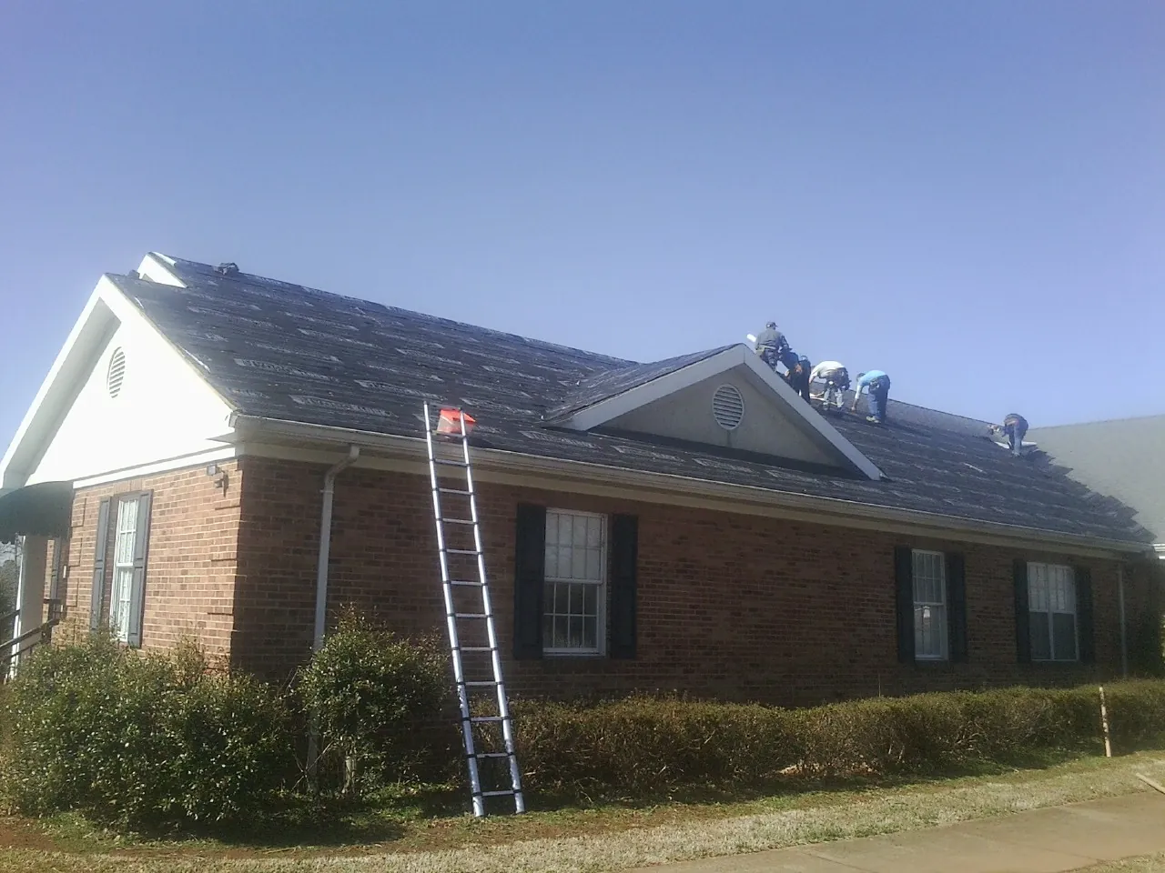 Crew tearing shingles off a brick ranch roof with a ladder set — Metal Roof Repair work by our crew in Dalton